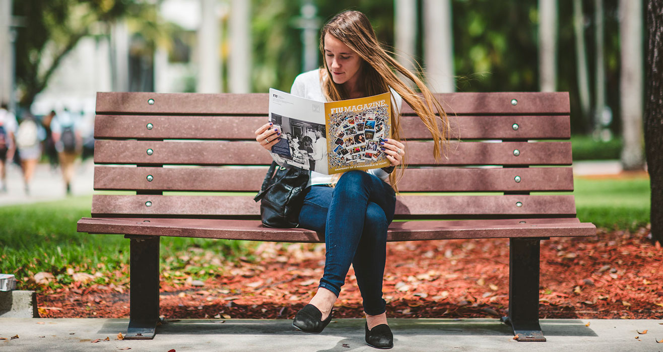 Student on bench reading FIU Magazine